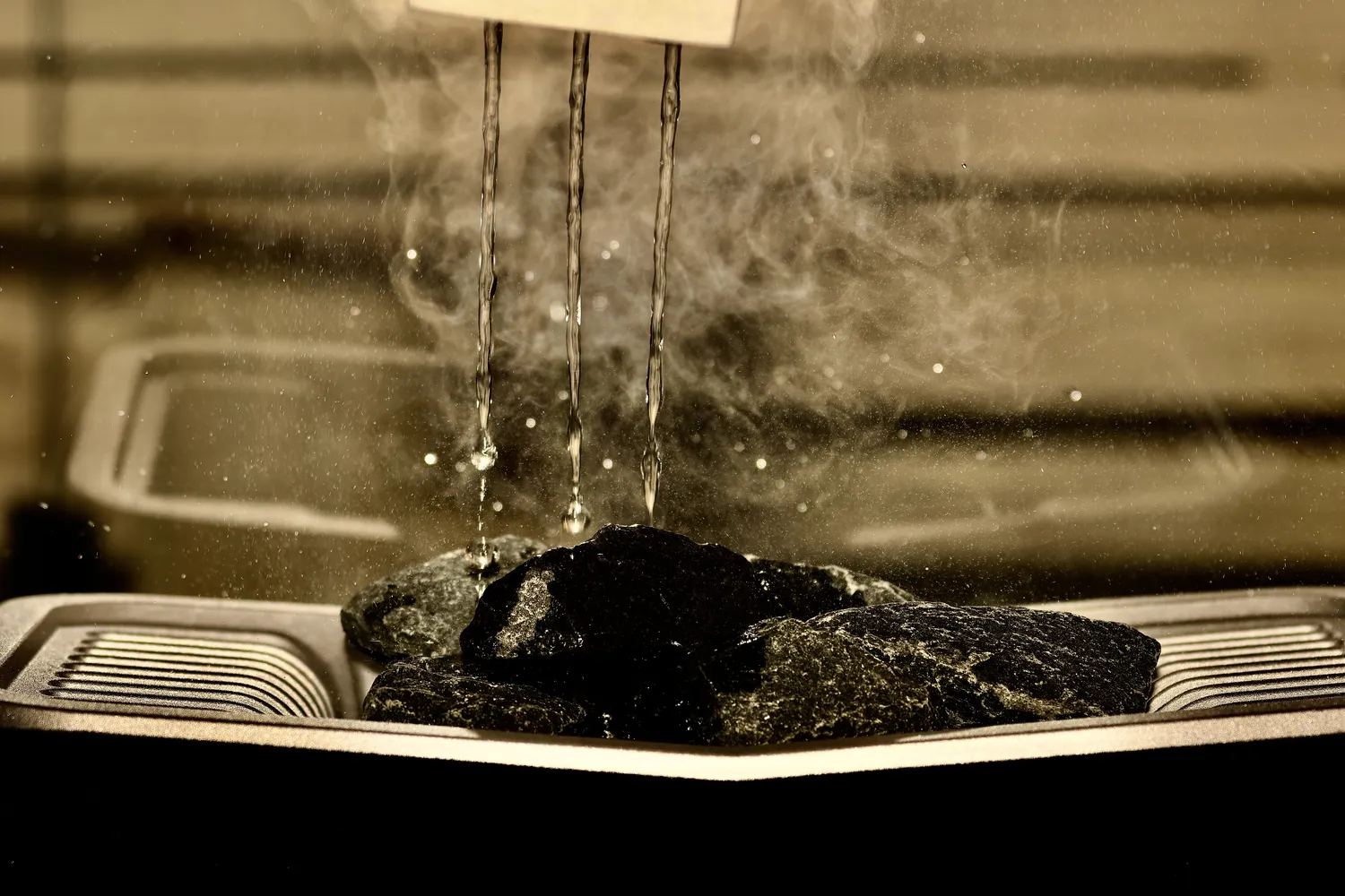 Sauna Stegmann - Wellness & More - Wasser trifft auf heiße Steine und Dampf steigt auf.