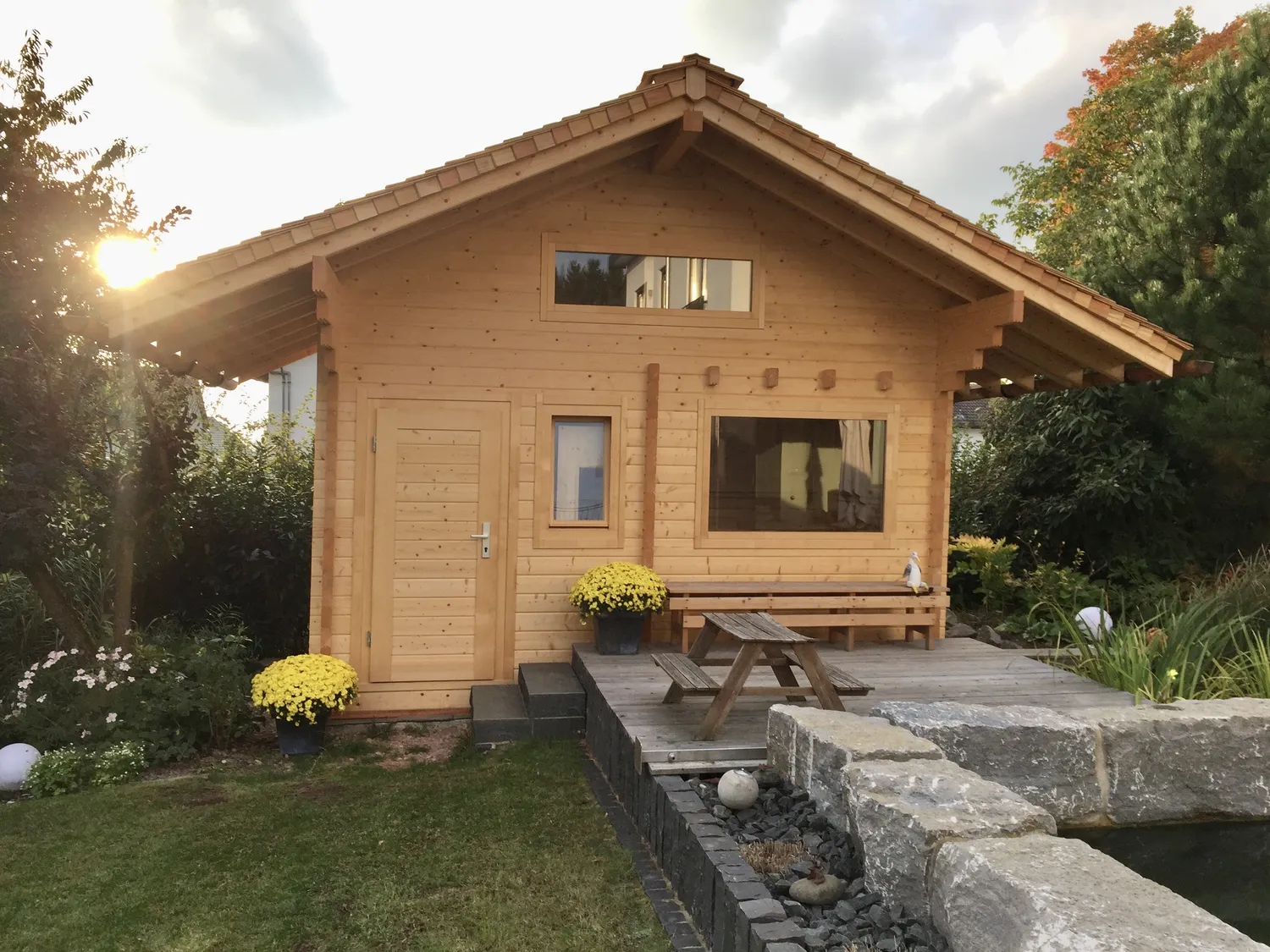 Sauna Stegmann - Wellness & More - Holzhaus mit Terrasse, Picknicktisch und Garten im Sonnenlicht